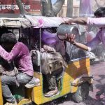 Un hombre echa una cubeta llena de color a un carro con gente en Mathura, India